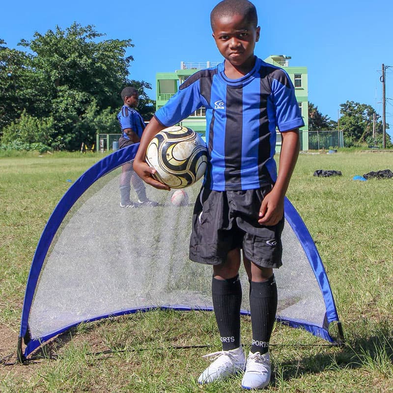 One player standing in front of the practice goal with a ball under his right arm